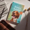 A képen az Értsd a kutyád című könyv látható a háttérben egy barna színű kutya.