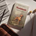 A képen A vizslatanító című könyv látható a háttérben egy magyar vizslával.