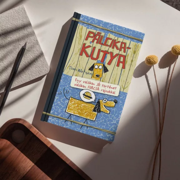 A képen a Pálcikakutya című könyv látható egy keverék kutyával a háttérben.