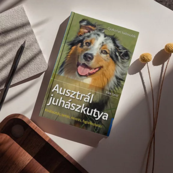 A képen az Ausztrál juhászkutya című könyv látható a háttérben egy ausztrál juhászkutya.
