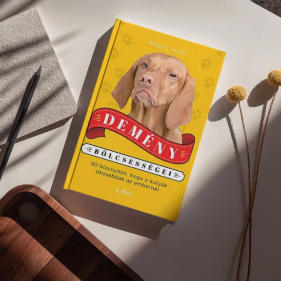 A képen a Demény bölcsességei című könyv látható a háttérben egy vizsla.
