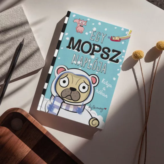 A képen az Egy mopsz naplója Kutya a hóban című könyv látható hóval a háttérben.