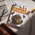 A képen a Jó kutya című könyv látható a háttérben egy malinois kölyök.