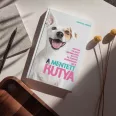 A képen A mentett kutya című könyv látható a háttérben egy kutyáját ölelő gazdival.