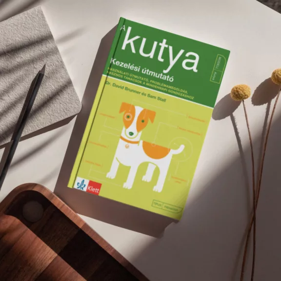 A képen A kutya Kezelési útmutató című könyv látható a háttérben egy kutyával.