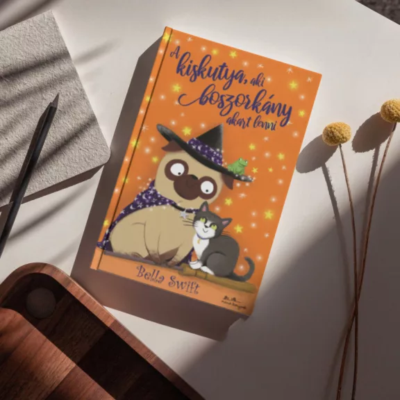 A képen A kiskutya aki boszorkány akart lenni című könyv látható a háttérben egy mopsz.