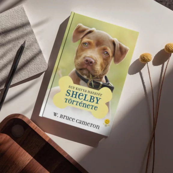 A képen az Egy kutya hazatér Shelby története című könyv látható a háttérben egy pitbull.