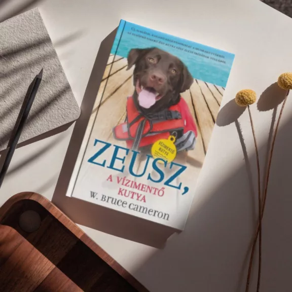 A képen Zeusz A vízimentő kutya című könyv látható a háttérben két kutyával.